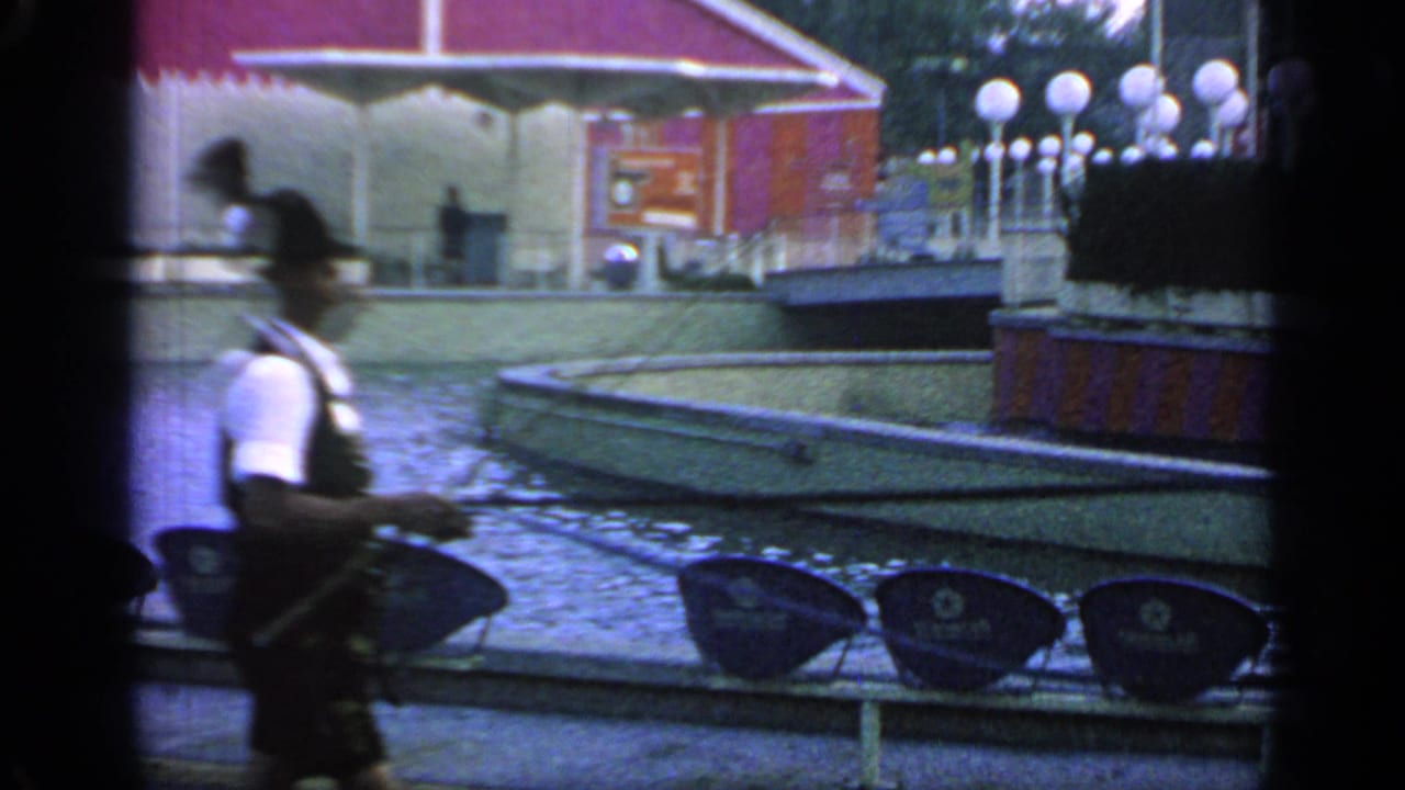 Man in dark shorts walks near blue seats and a red fairground building.