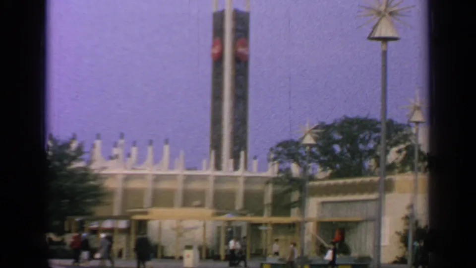 A wider 1964 Flushing Meadows view shows a tall fairground tower, pavilion rooflines, trees, lamps, and visitors beneath a clear sky.