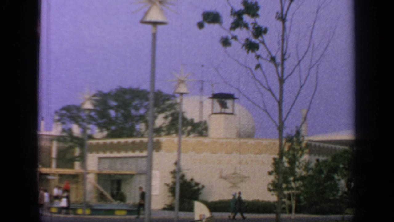 1964 Flushing Meadows exterior with a pale pavilion wall, rounded roof form, star lamps, trees, and visitors along the path.