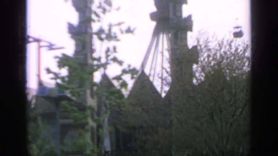 1964 World's Fair fairground view with cable car structure, trees, and the Indonesia Pavilion roof peaks in soft focus.