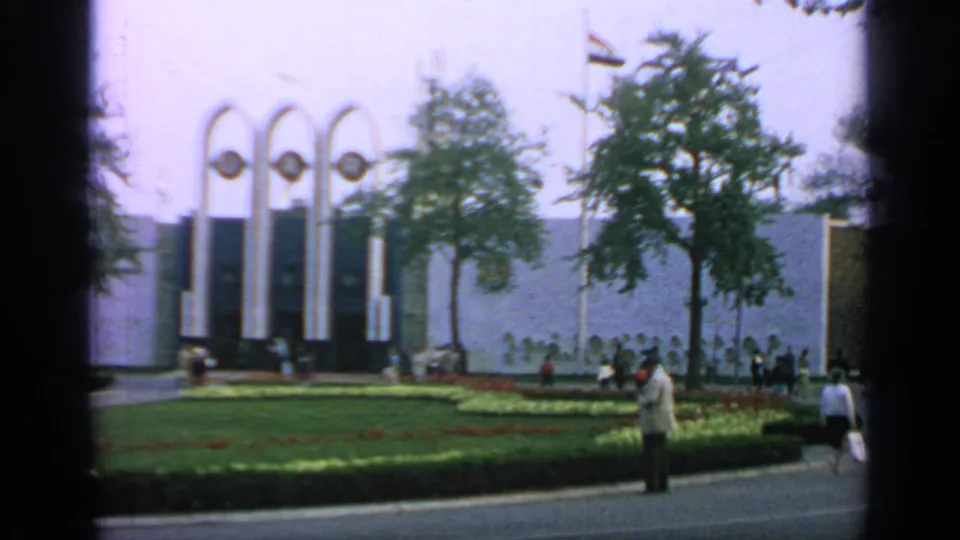 Handheld 8mm view of the U.A.R. pavilion area at the 1964 New York World's Fair, with visitors beside gardens and trees.