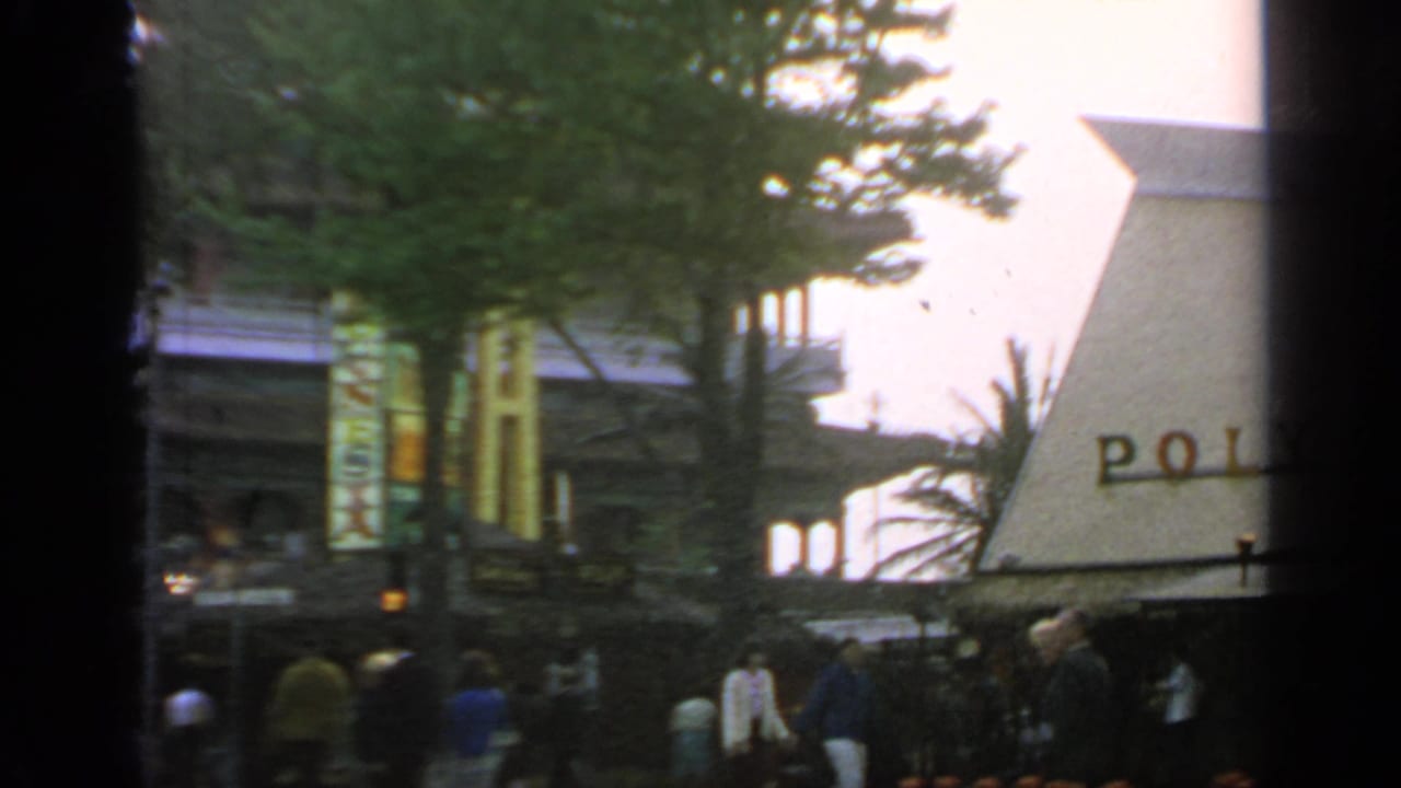 Polynesian Restaurant exterior partly framed by trees with visitors walking nearby.