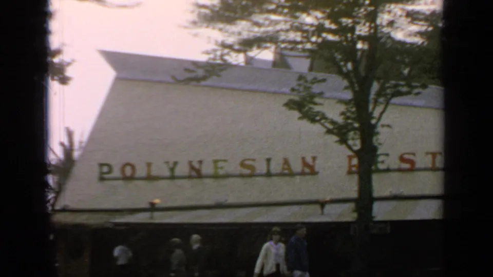 1964 Flushing Meadows view of a Polynesian restaurant exterior with trees, striped awning, and pedestrians passing below the sign.