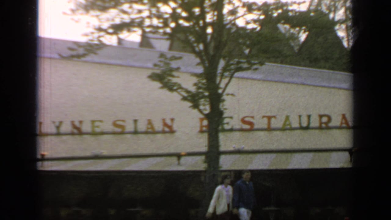 Closer exterior view of the Polynesian Restaurant sign with trees and two pedestrians near the entrance.