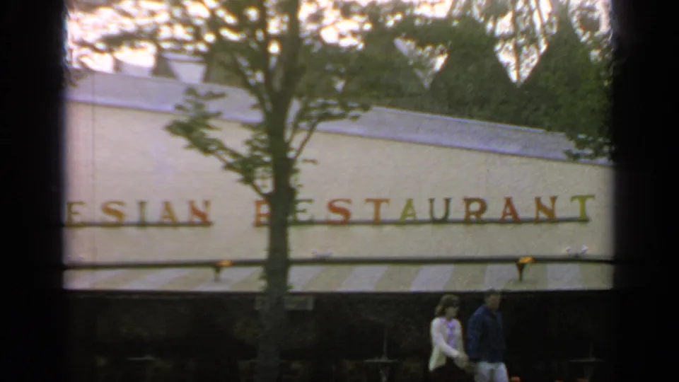 1964 Flushing Meadows footage frames the Polynesian Restaurant lettering behind a tree, with awning stripes and visitors below.