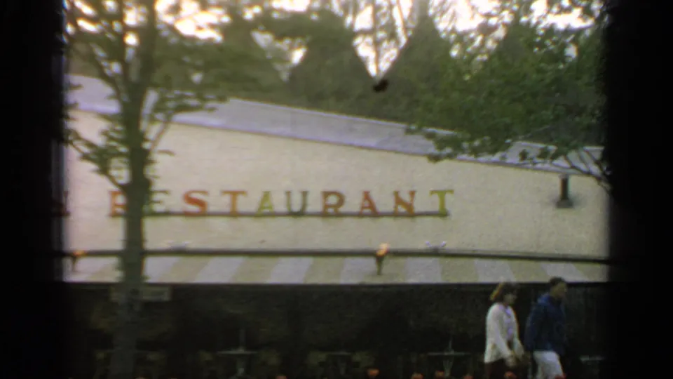 1964 Flushing Meadows restaurant exterior with partial Polynesian Restaurant lettering, trees above the awning, and a couple walking past.