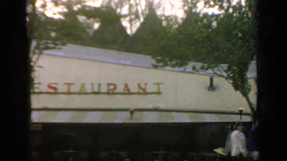 1964 Flushing Meadows view of a red restaurant sign on a pale exterior, partly obscured by trees and film-edge shadows.