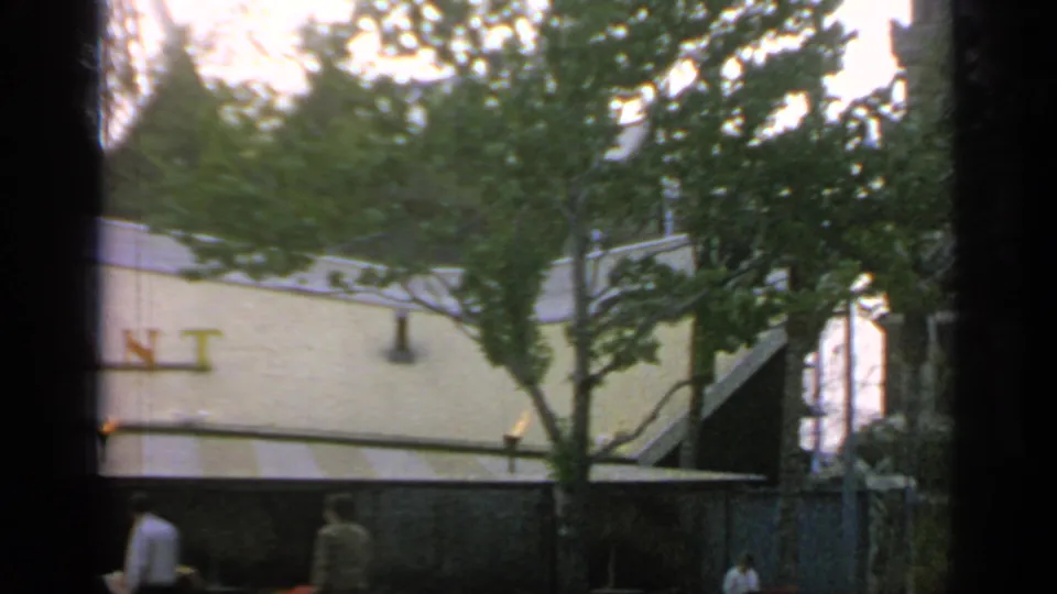 The camera view shifts along the restaurant wall, leaving only part of the red sign visible behind trees.