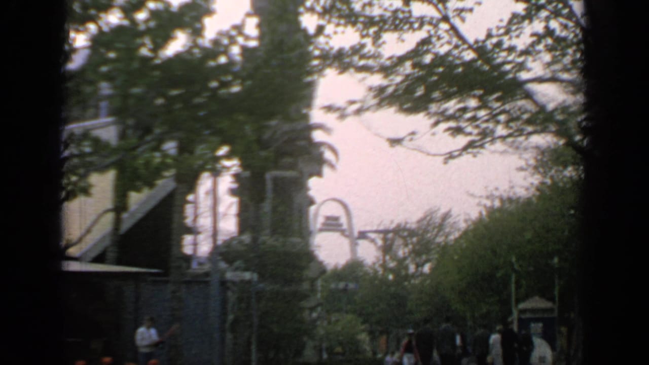 Arched building behind trees with people walking along the fairground path.