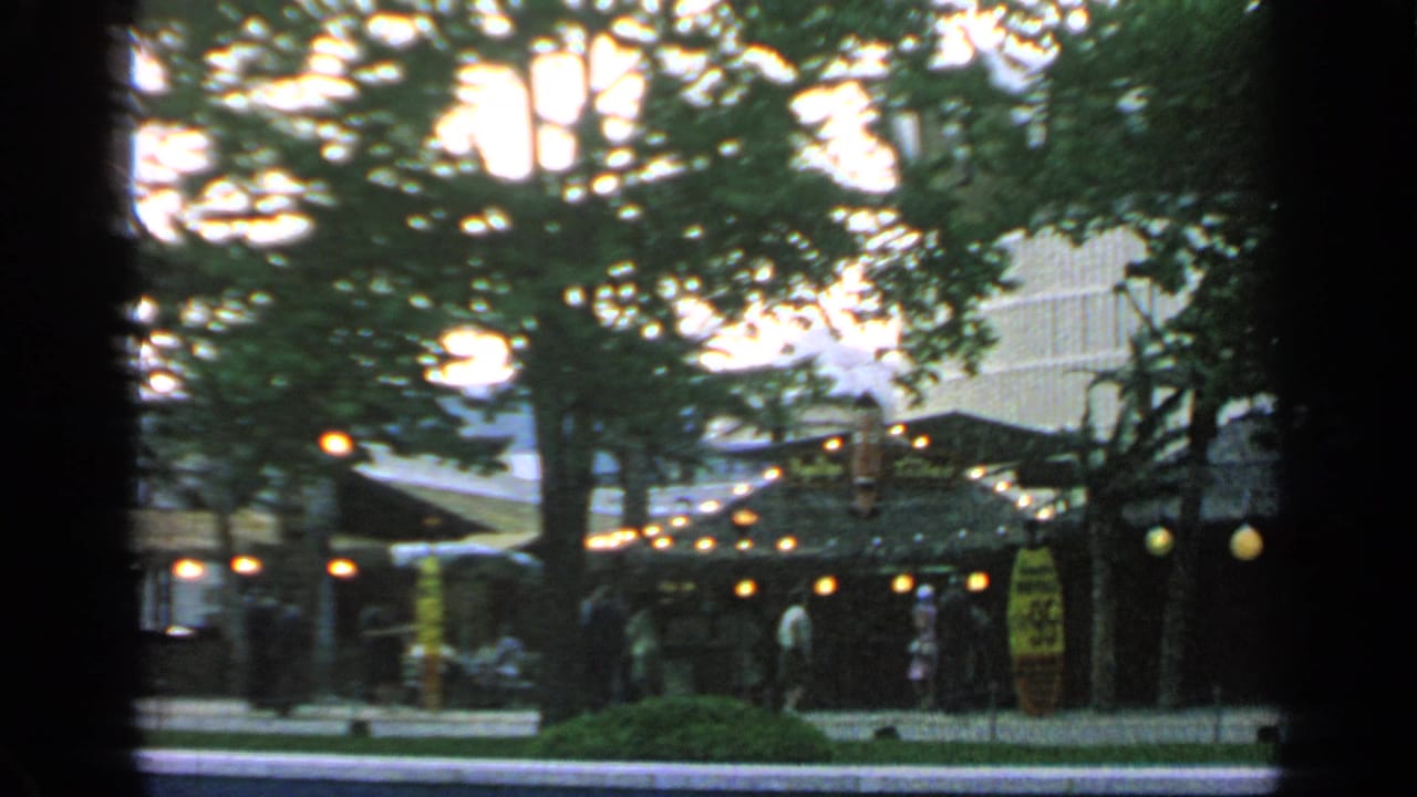 Thatched market huts with lanterns under trees and people walking nearby.