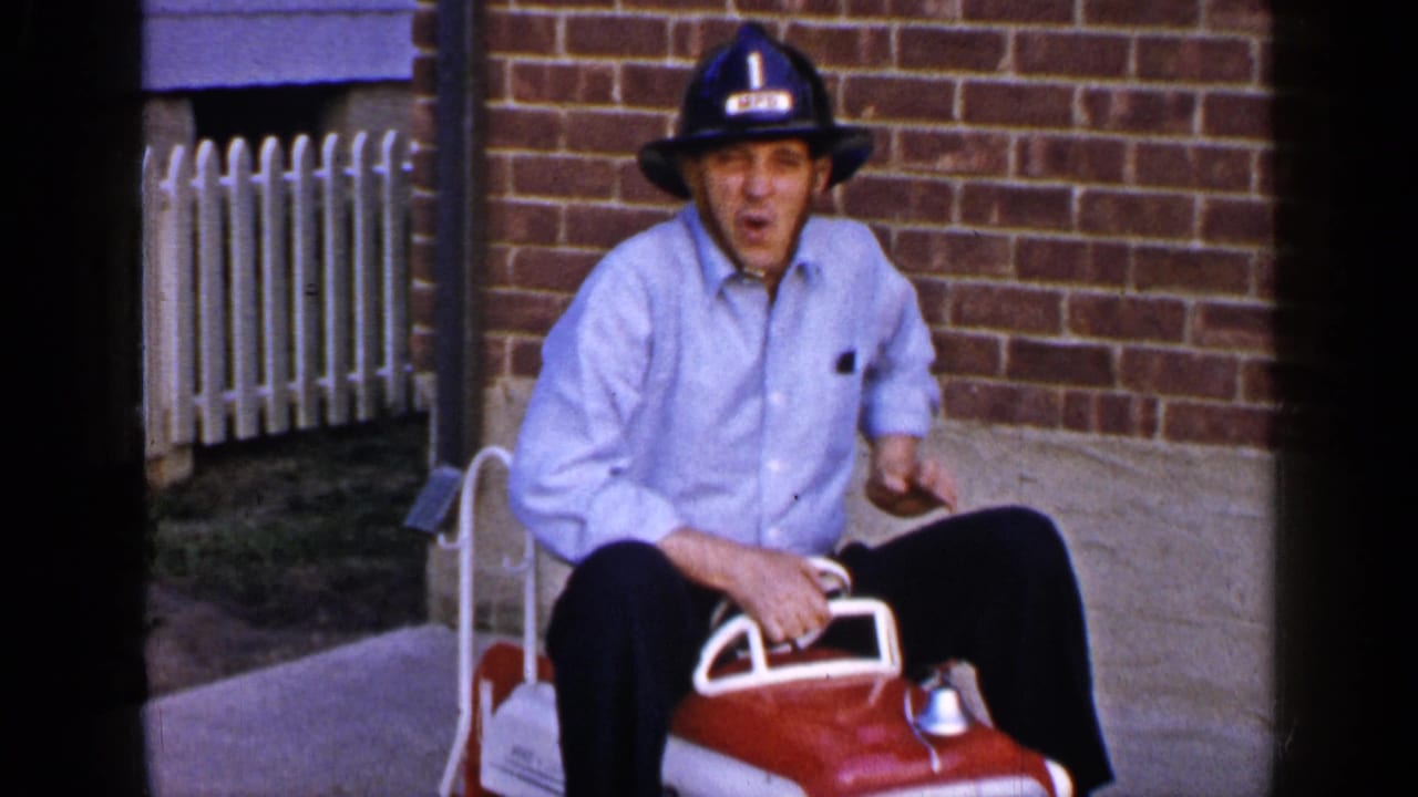 Man wearing a black helmet sits on a red and white toy fire truck.