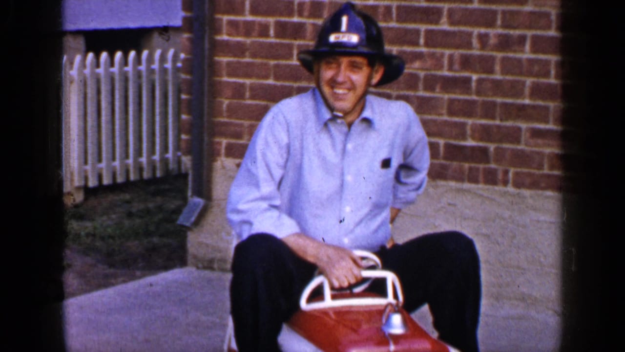 The final frame shows the helmeted man smiling on the red toy fire truck, framed by brickwork, concrete, and a white fence.
