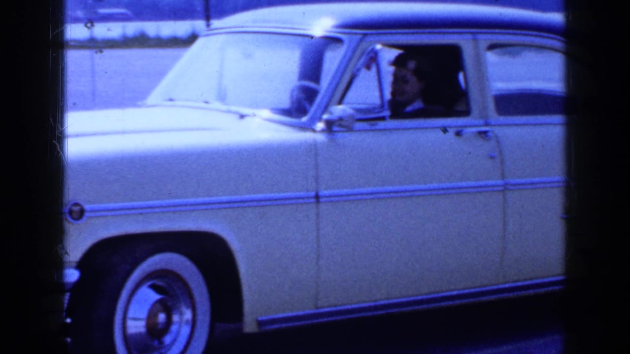Yellow vintage car passing close to camera with a woman visible through the driver-side window.