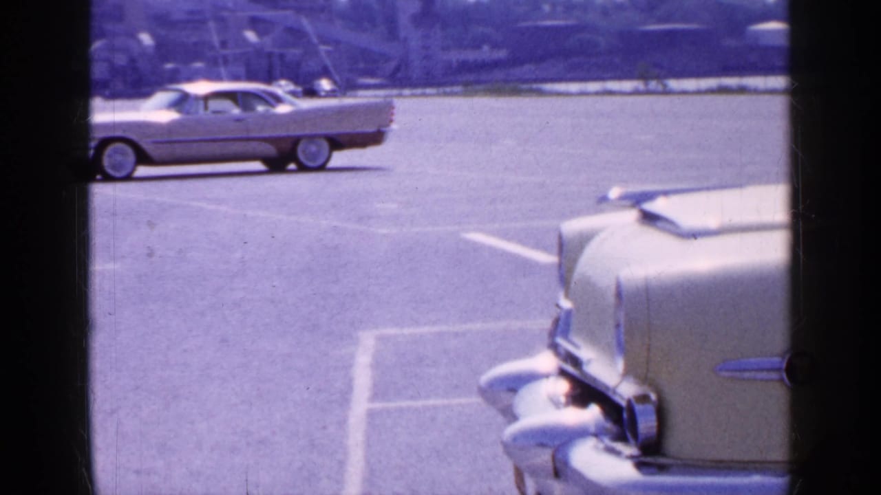 Waterfront parking area with mid-century cars and a partial car foreground.