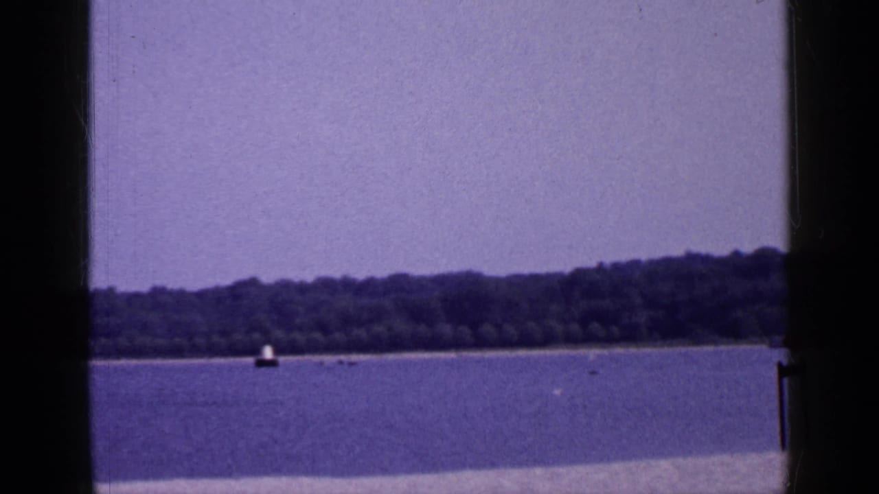 Wide water view with distant shore, small buoy, and dark vertical film borders.