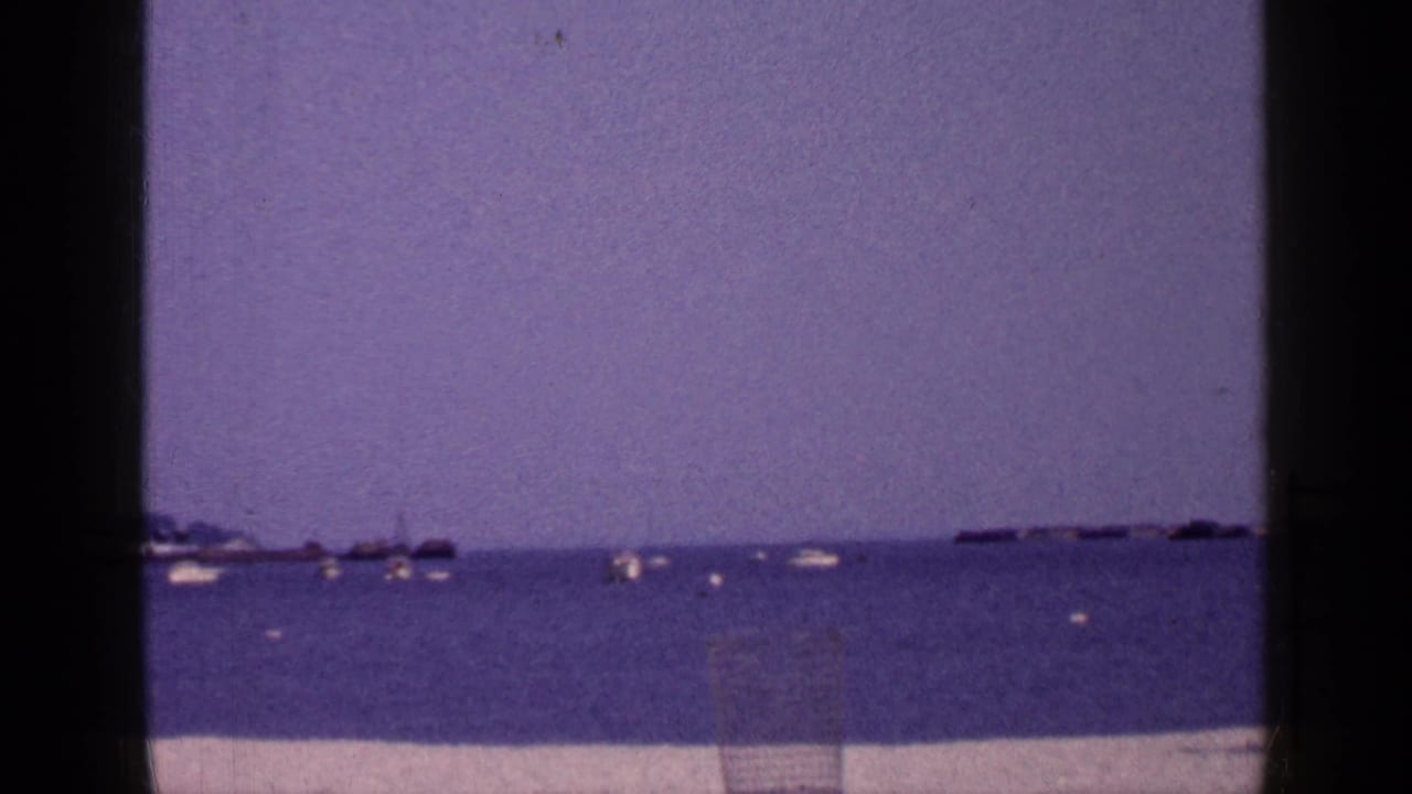 Long Island 8mm shoreline view with open water, distant small boats, a pale strip of sand, and visible vintage film color shift.