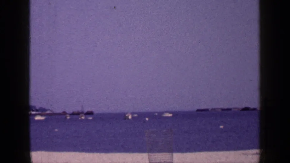 Long Island 8mm shoreline view with open water, distant small boats, a pale strip of sand, and visible vintage film color shift.