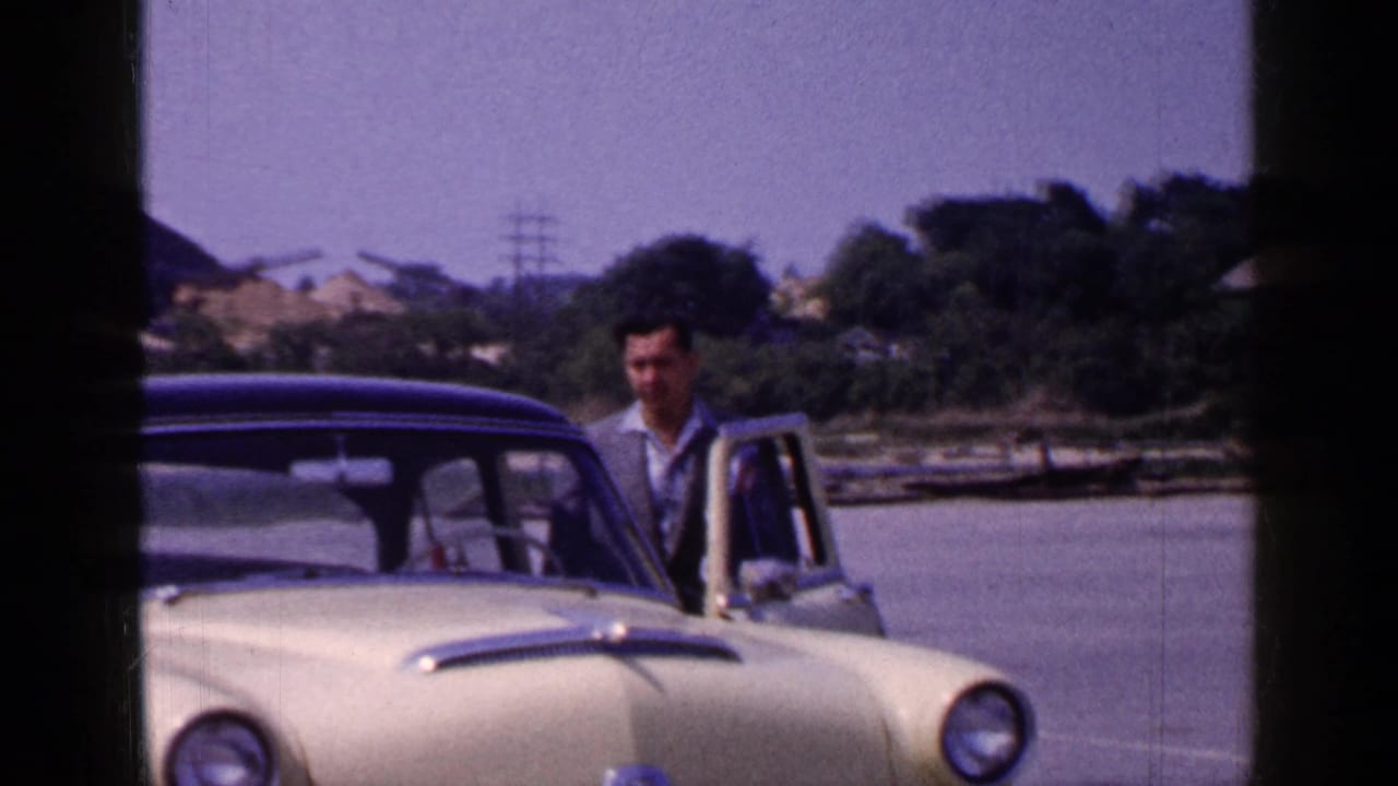 Adult man beside the open driver door of a yellow mid-century sedan near a Long Island waterfront in 1965.
