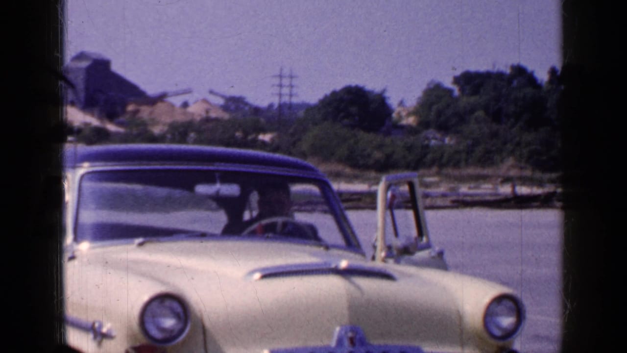Yellow sedan with blue roof faces the camera while the driver door remains open near the Long Island waterfront setting.