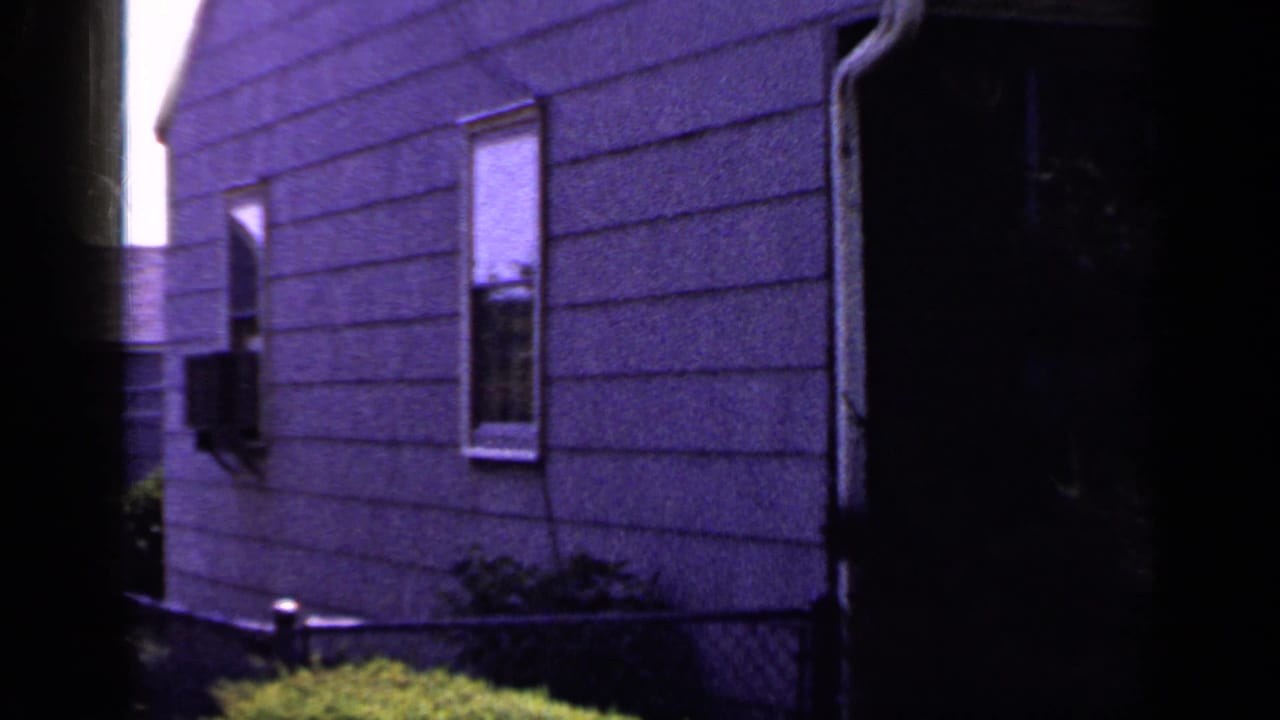 1965 home-movie frame shifts to a purple-tinted residential exterior with shingle siding, windows, foundation area, grass, and a dark doorway.