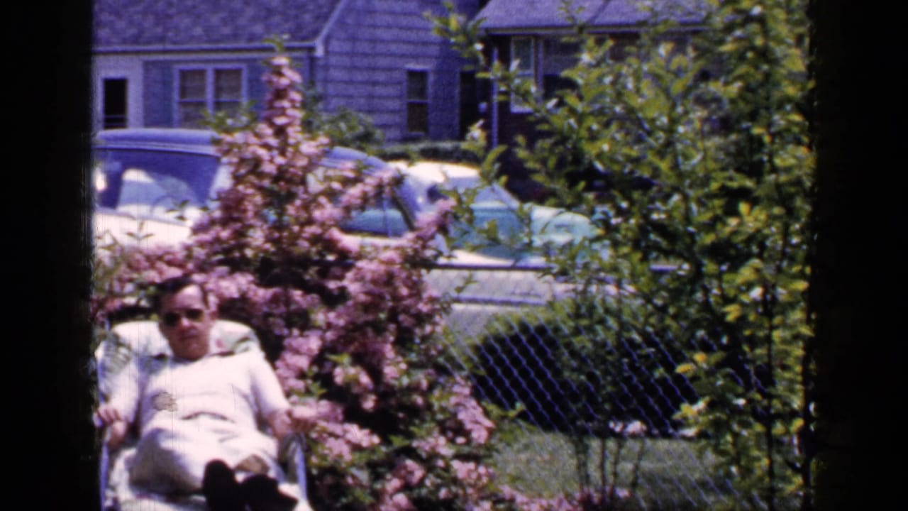Man in sunglasses reclines in a lawn chair beside pink flowers and shrubs.