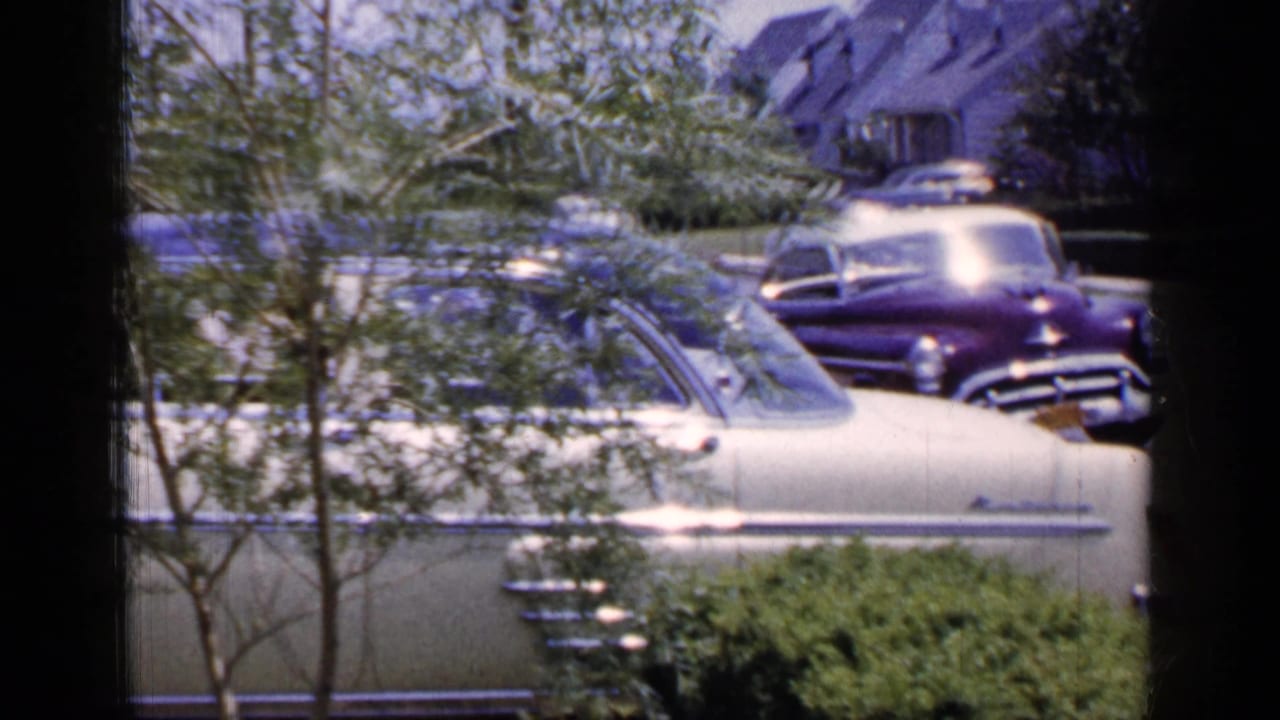 Cream-colored sedan in foreground with a purple car parked farther along the street.