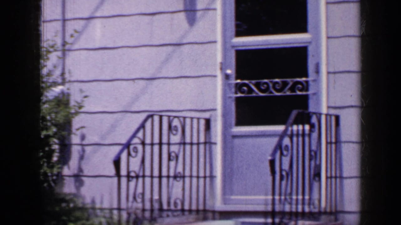 White door, black iron railings, grey siding, and front steps.