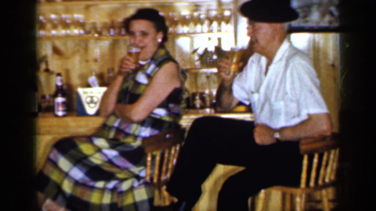 1965 Long Island tavern interior with an older woman in a plaid dress and a man in a white shirt and dark hat drinking.