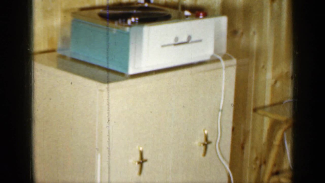 Portable record player on a cabinet against wood-paneled walls.