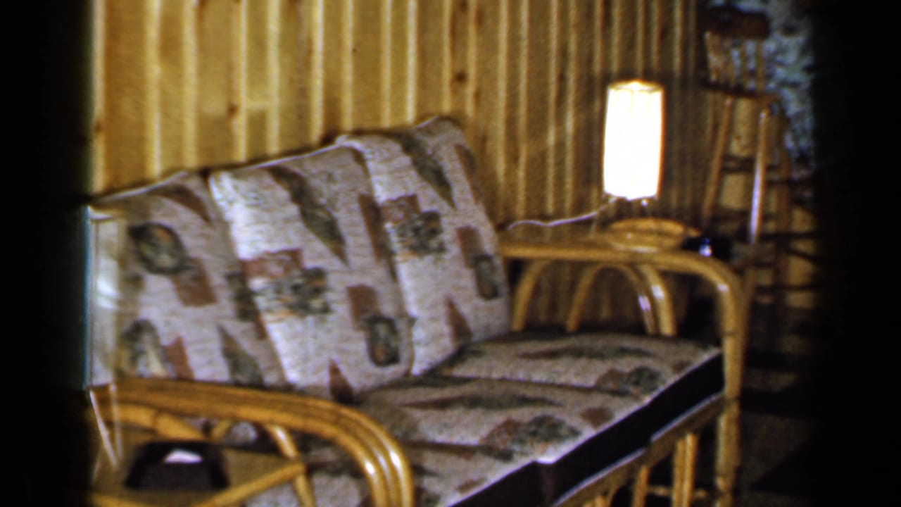 Rattan sofa and lamp framed closer against vertical wood paneling.