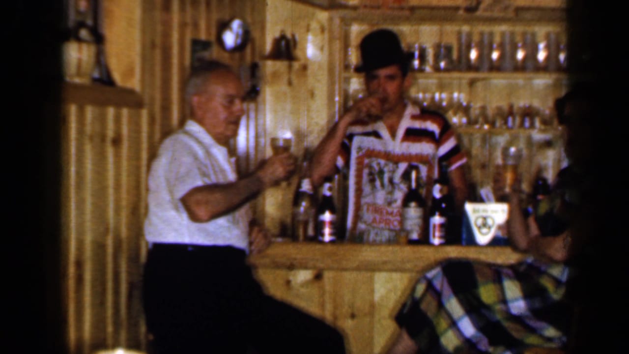 Older man and bartender raise glasses at a rustic wooden bar.