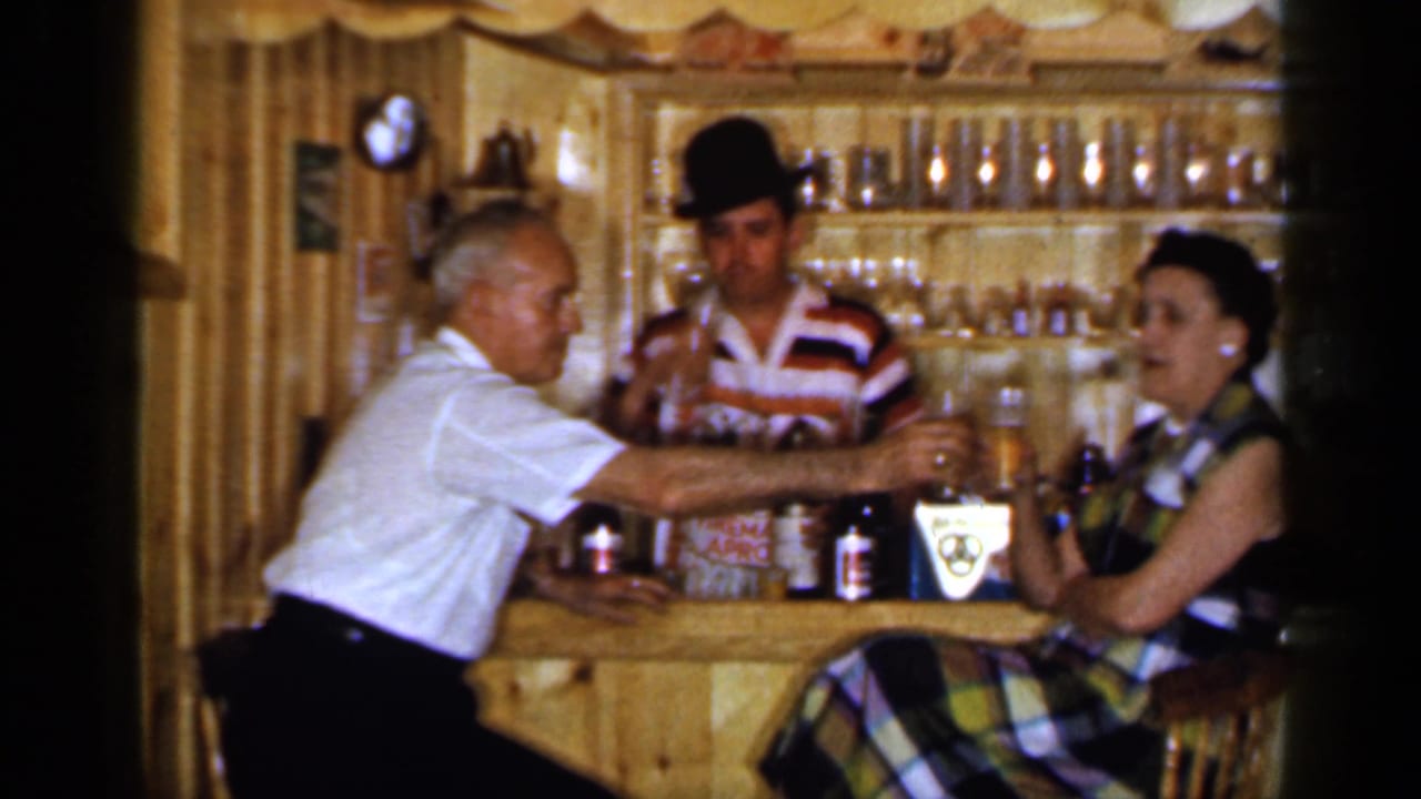 Man reaches across the bar to toast a seated woman while the bartender watches.