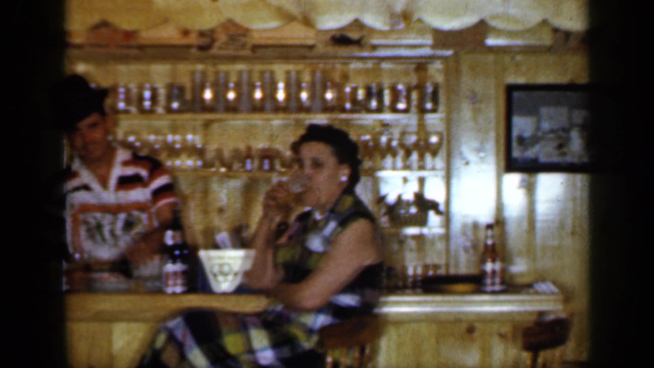 Woman seated at a wooden tavern bar while a bartender stands nearby.
