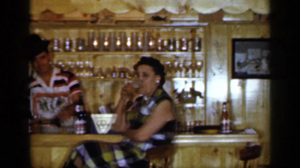 1965 Long Island tavern interior with a woman drinking at the bar and a bartender in a striped shirt behind the counter.