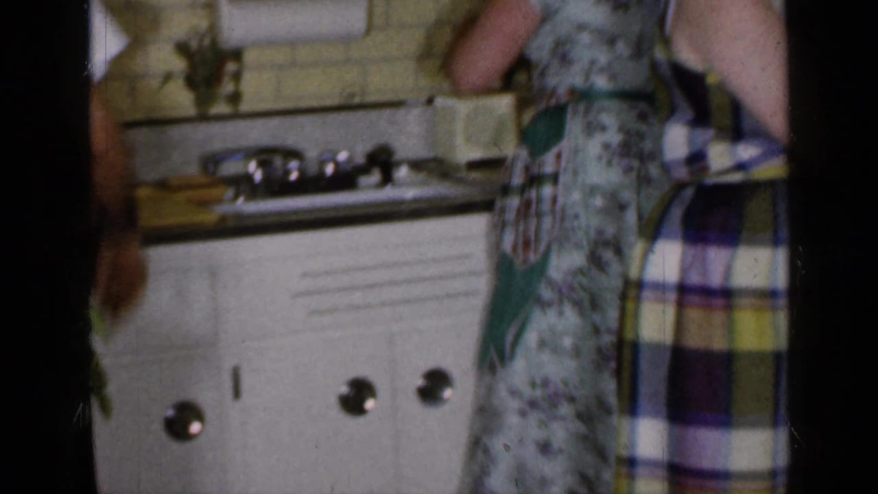 Two women standing by a kitchen counter with sink, cabinets, and tiled backsplash visible.