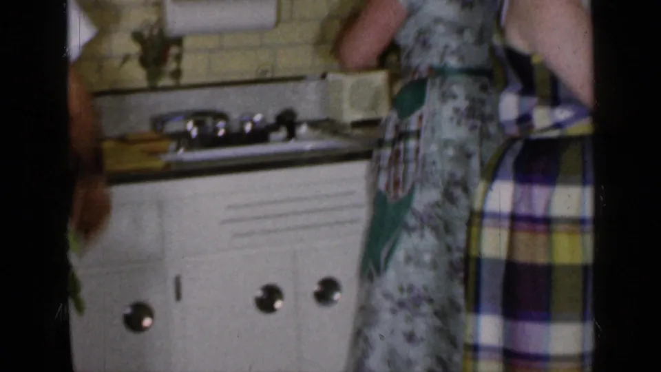 1965 Long Island home-movie frame showing two women near a kitchen sink and counter in a private interior.