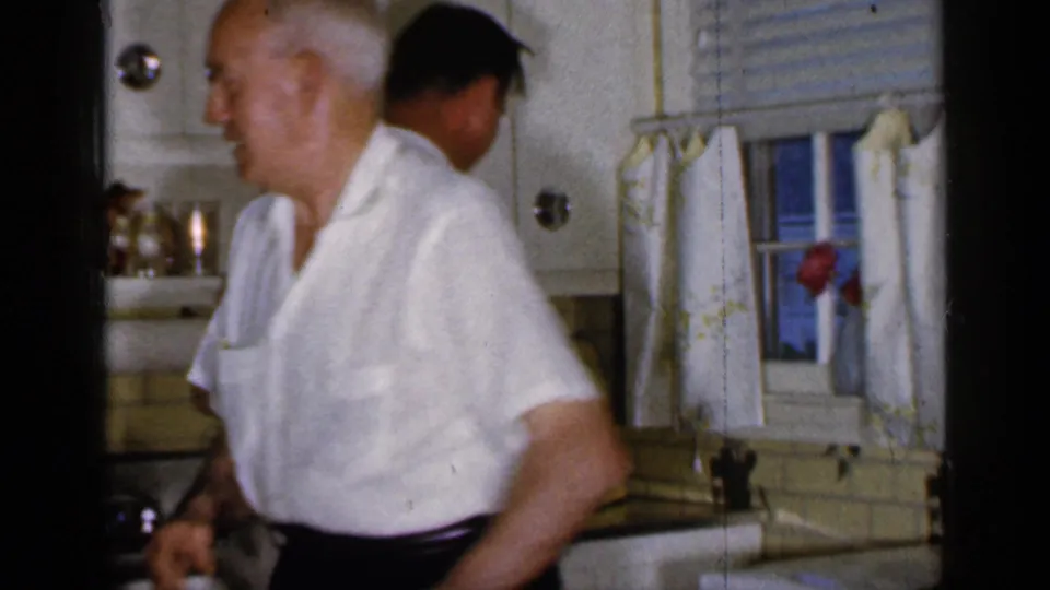 In the Long Island kitchen, a man in a white shirt passes in front of the sink area as another adult is partly visible behind him.