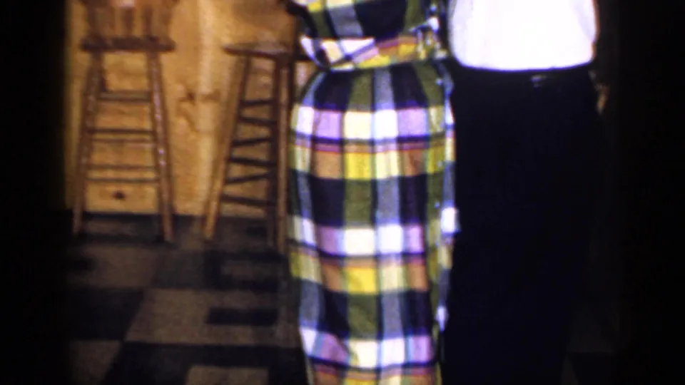 The couple continues dancing in the 1965 Long Island bar scene, with the plaid dress and dark trousers prominent.