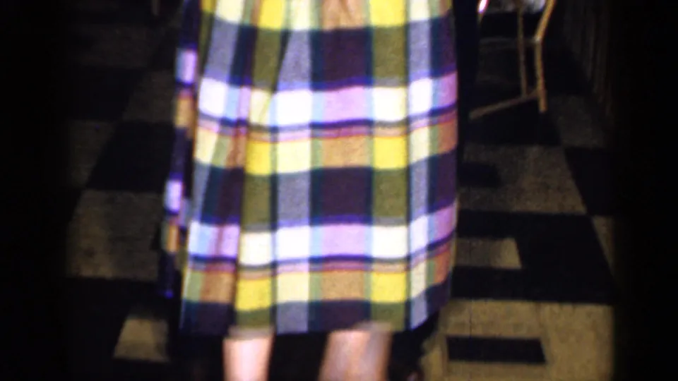 A cropped 8mm frame shows the woman's plaid dress as she dances with a man in the Long Island bar interior.
