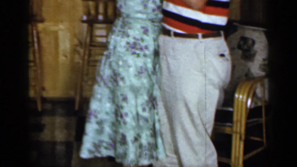 A couple dances beside the wood-paneled bar, with the woman's green floral dress and the man's striped polo visible in the 1965 footage.