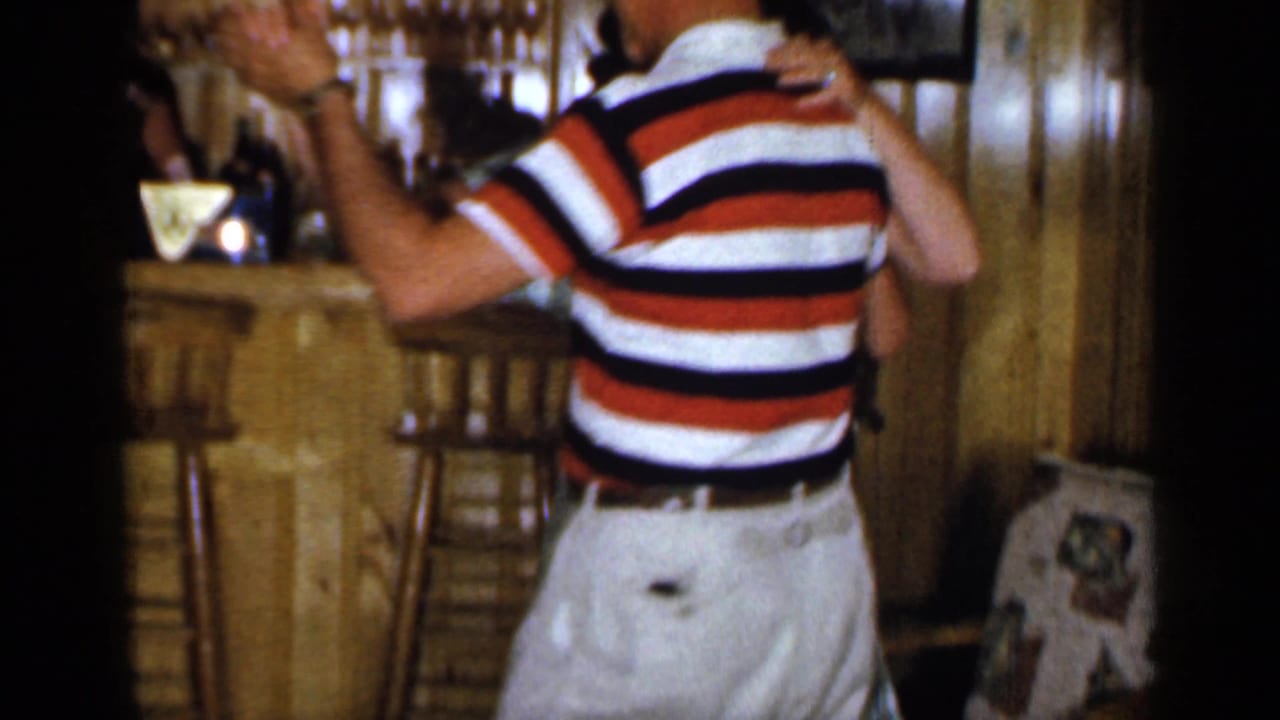 Adult couple dancing near a wood bar, with the man in a striped shirt and hat.