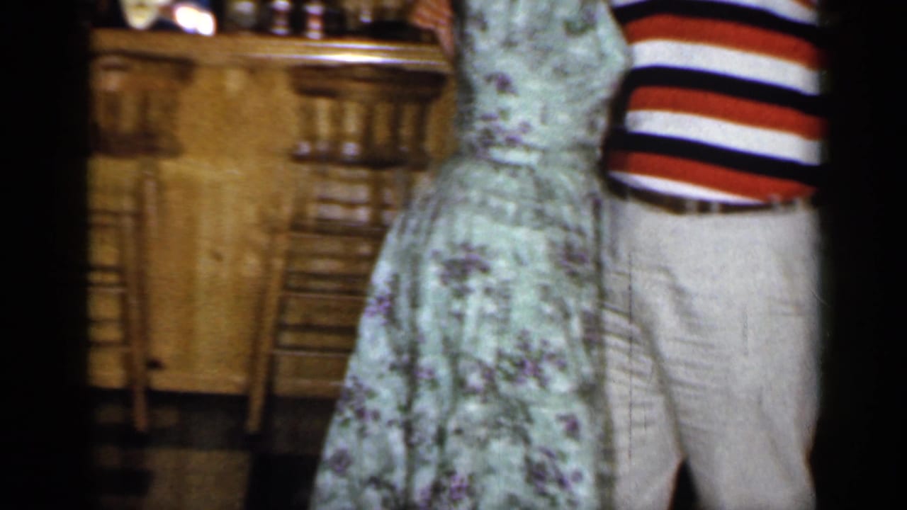 Couple dancing in front of a wood-paneled basement bar, partially cropped by the frame.