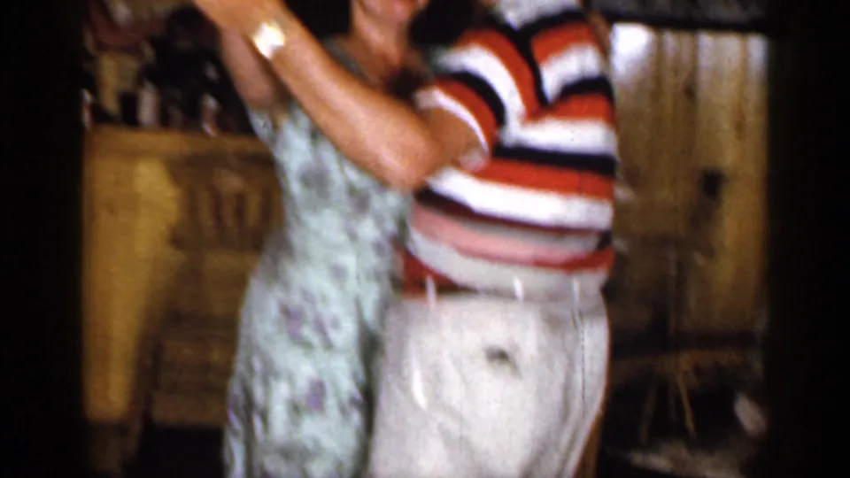 The handheld 8mm frame catches the couple mid-dance, cropped close against the warm basement bar interior.