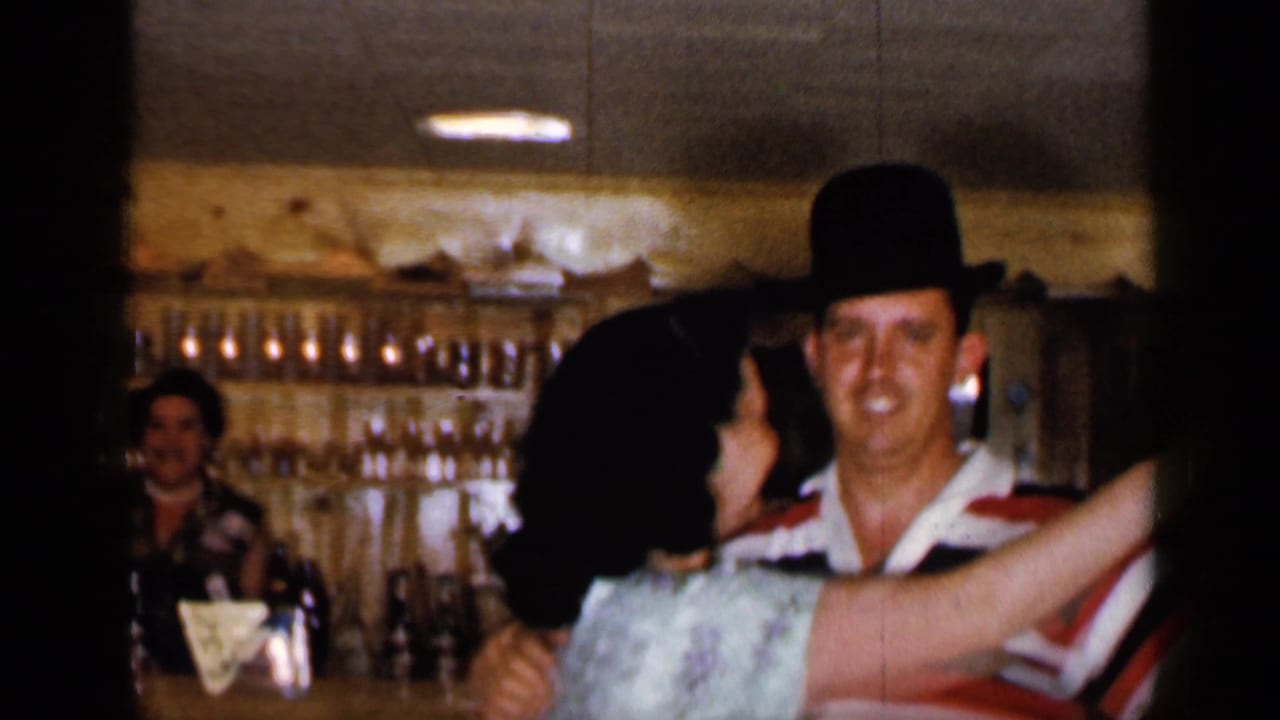Couple dancing closely in a wood-paneled bar interior with shelves behind them.