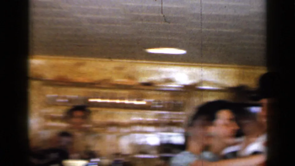 Motion blur trails the dancing couple as they move through the wood-paneled Long Island bar interior in this 1965 home-movie frame.