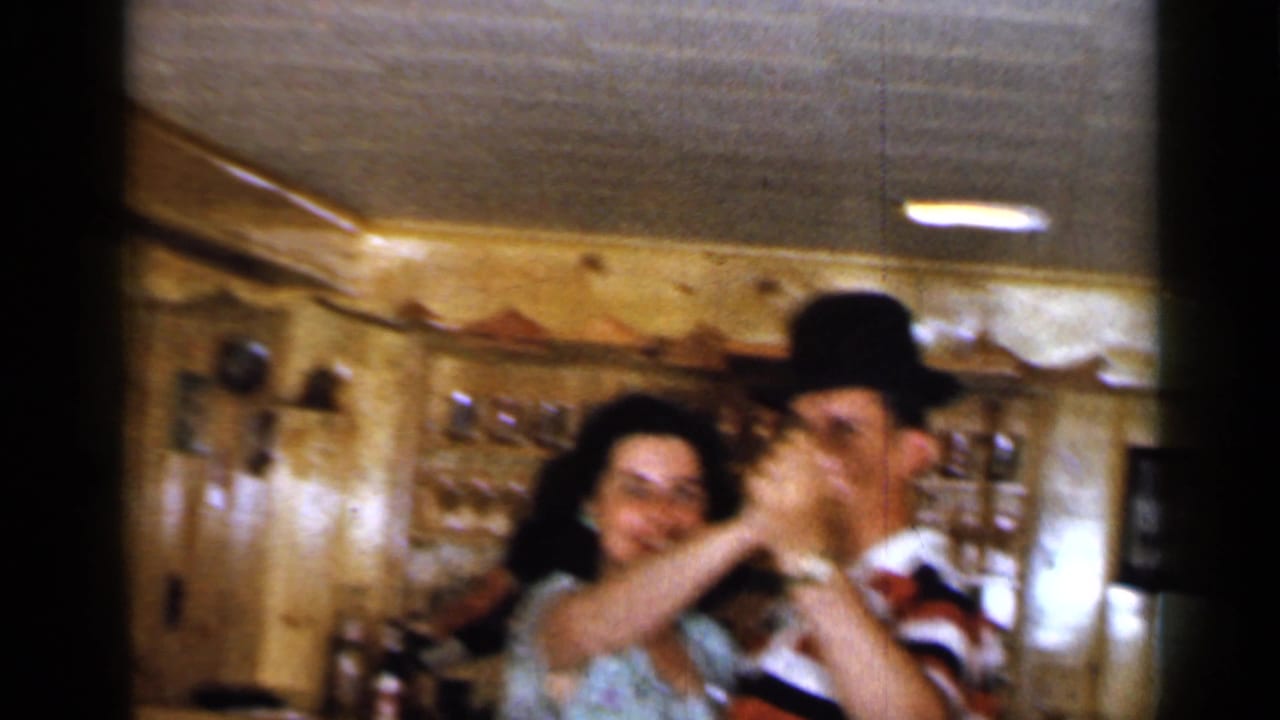 Dancing couple moves across a small bar interior with wood walls and ceiling light visible.
