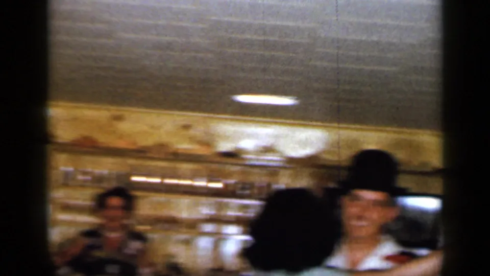 At the end of the clip, the man in the dark hat smiles during the dance as the bar counter and another adult remain visible behind him.