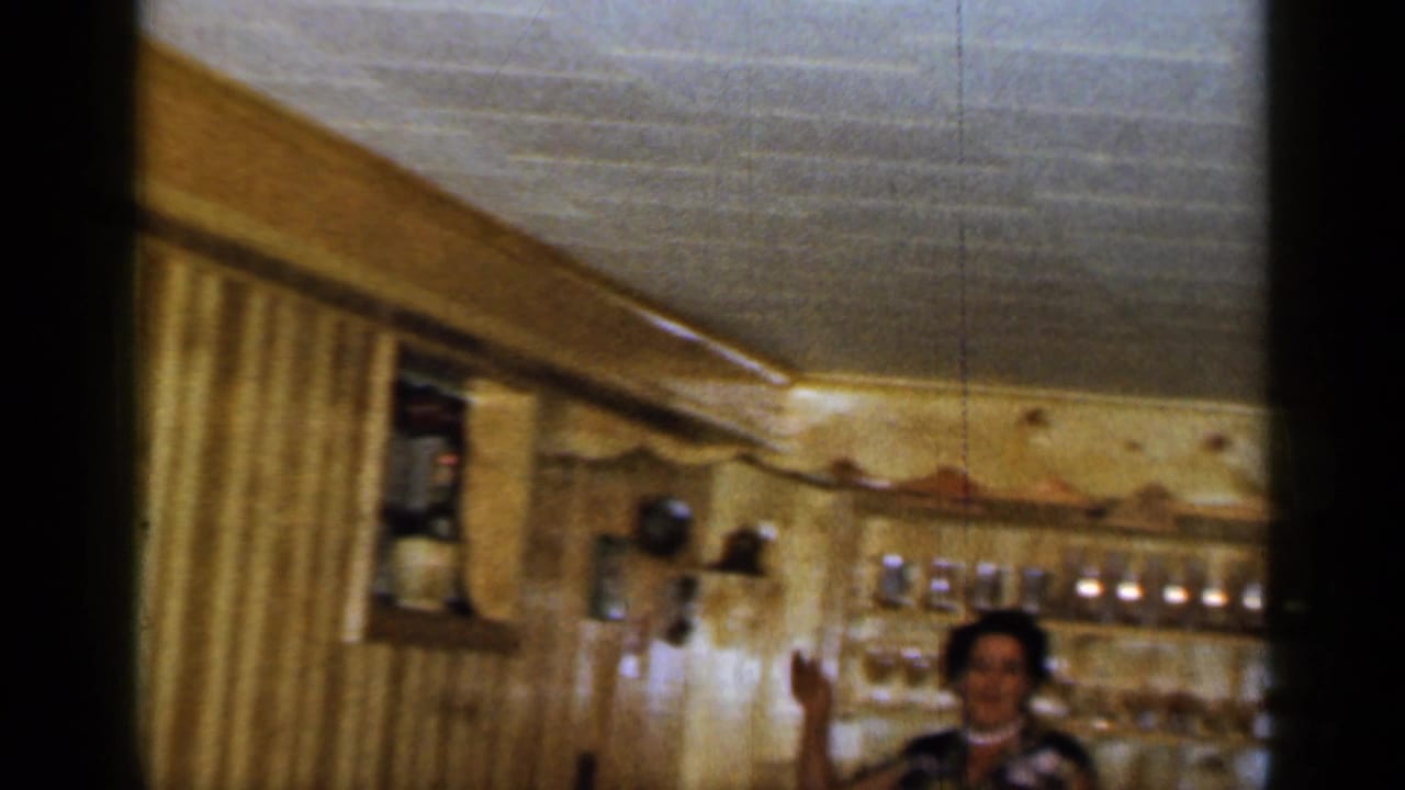 Wood-paneled interior with curtains and a person visible near shelves in the background.