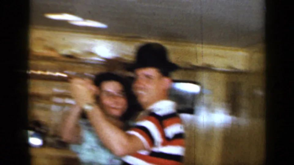 The couple continues dancing in the 1965 Long Island home movie, with motion blur from the handheld 8mm camera.