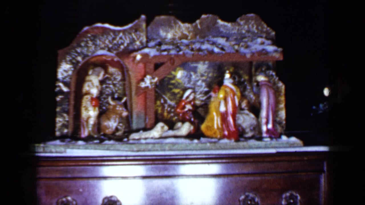 Ceramic nativity scene on a dark wooden cabinet with figures, animals, and a snowy stable roof.